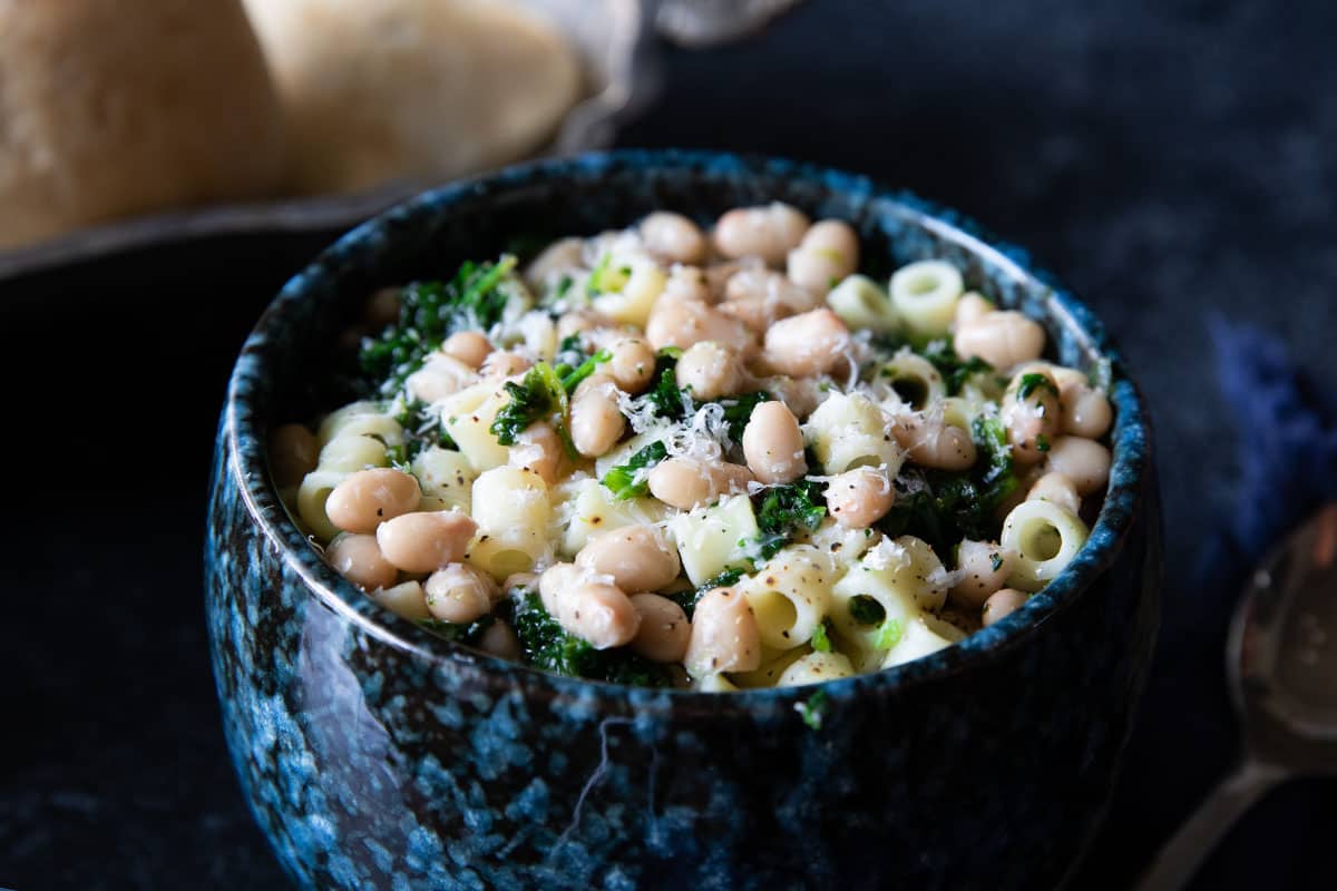 a close up of a bowl of white bean soup piled high with pasta and spinach