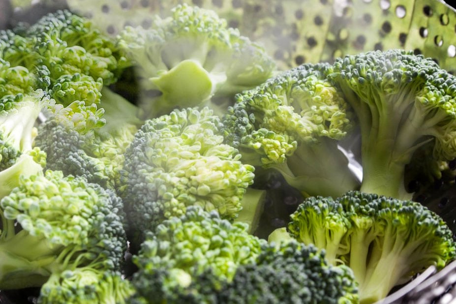 A close up of broccoli cooking in s steamer surrounded by steam