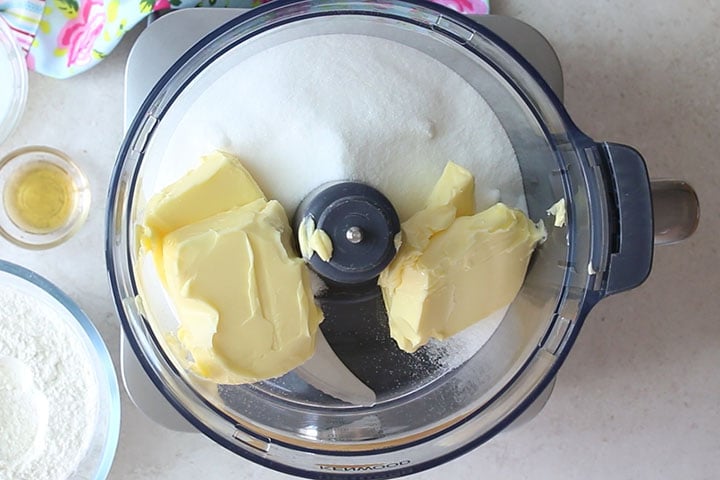 The butter and sugar added to a food processor bowl