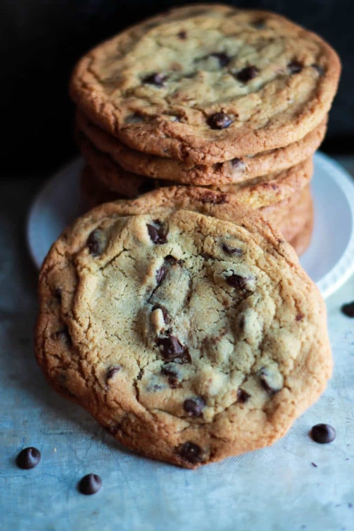 A plate of chocolate chip cookies stacked high on top of each other with on leaning against the stack