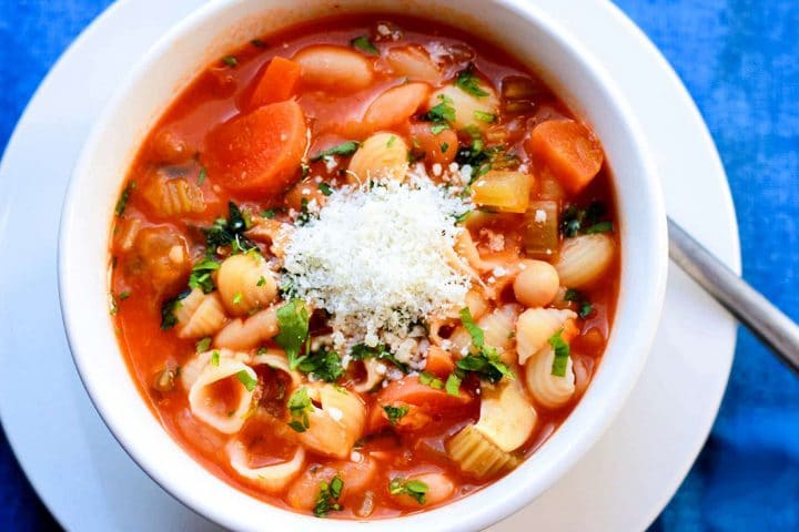 A close up view of a bowl of Pasta Fagioli with grated cheese and parsley on top