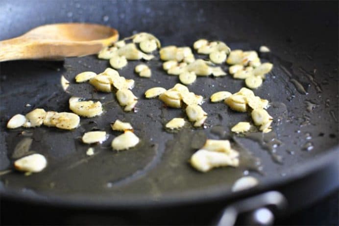 A pan with sliced garlic cooking in olive oil.
