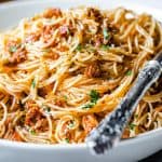 A close up photo of a plate of angel hair pasta with pesto sauce sprinkled with grated cheese and chopped parsley