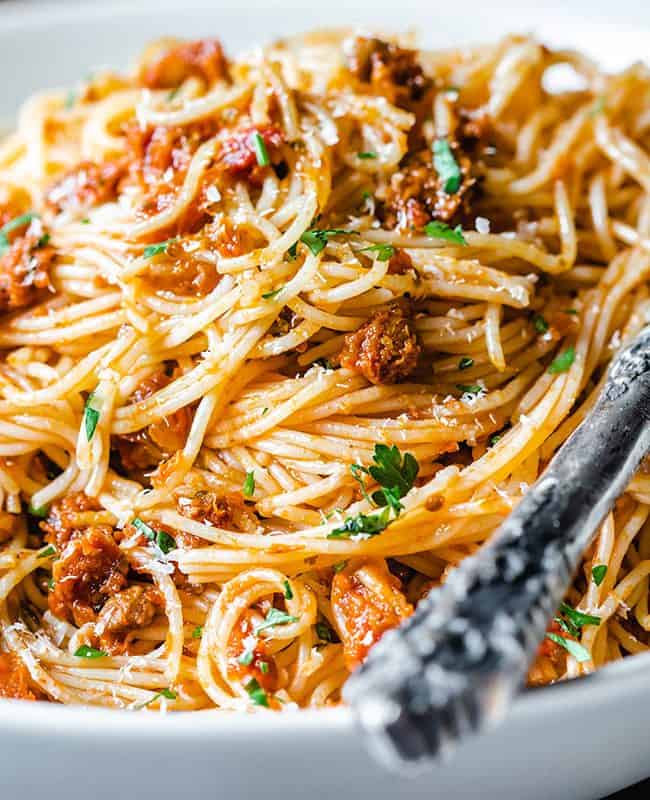 A close up photo of a plate of angel hair pasta with pesto sauce sprinkled with grated cheese and chopped parsley