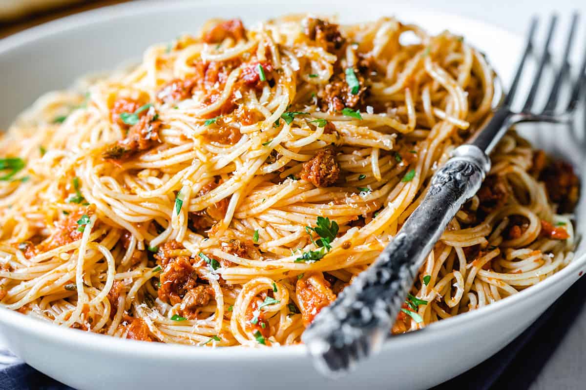 A close up photo of a plate of angel hair pasta with pesto sauce sprinkled with grated cheese and chopped parsley