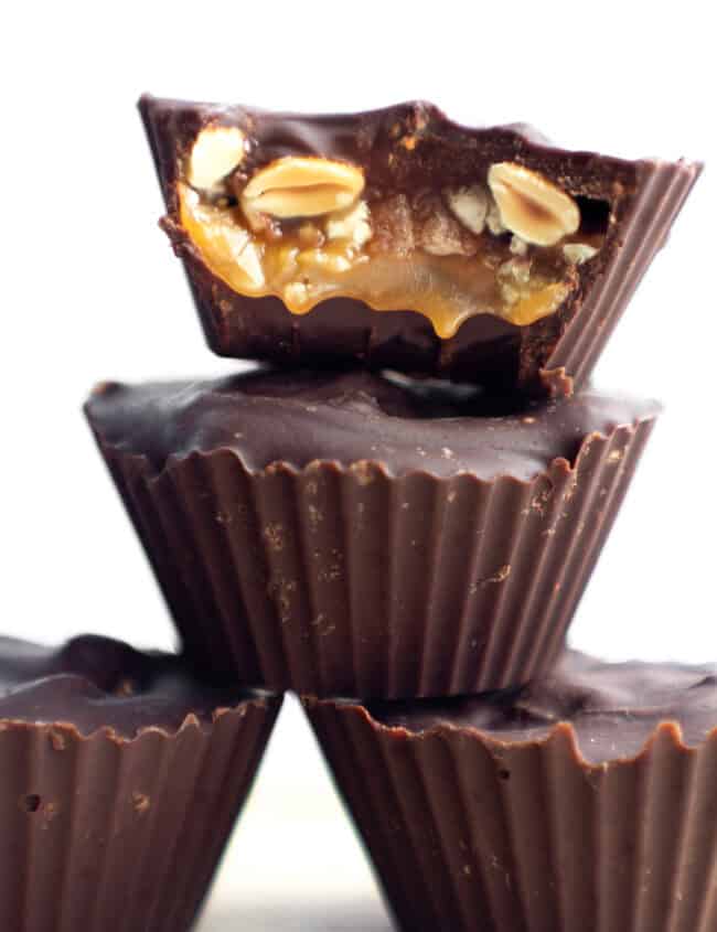 4 homemade snickers cups candies with one cut open to see the caramel and peanuts inside