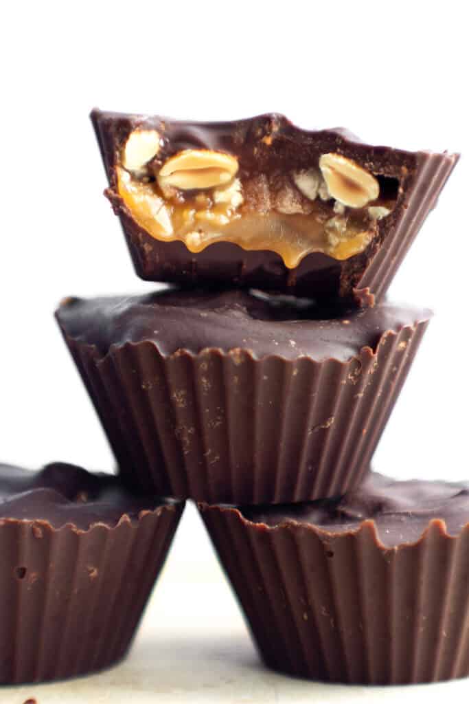 4 homemade snickers cups candies with one cut open to see the caramel and peanuts inside