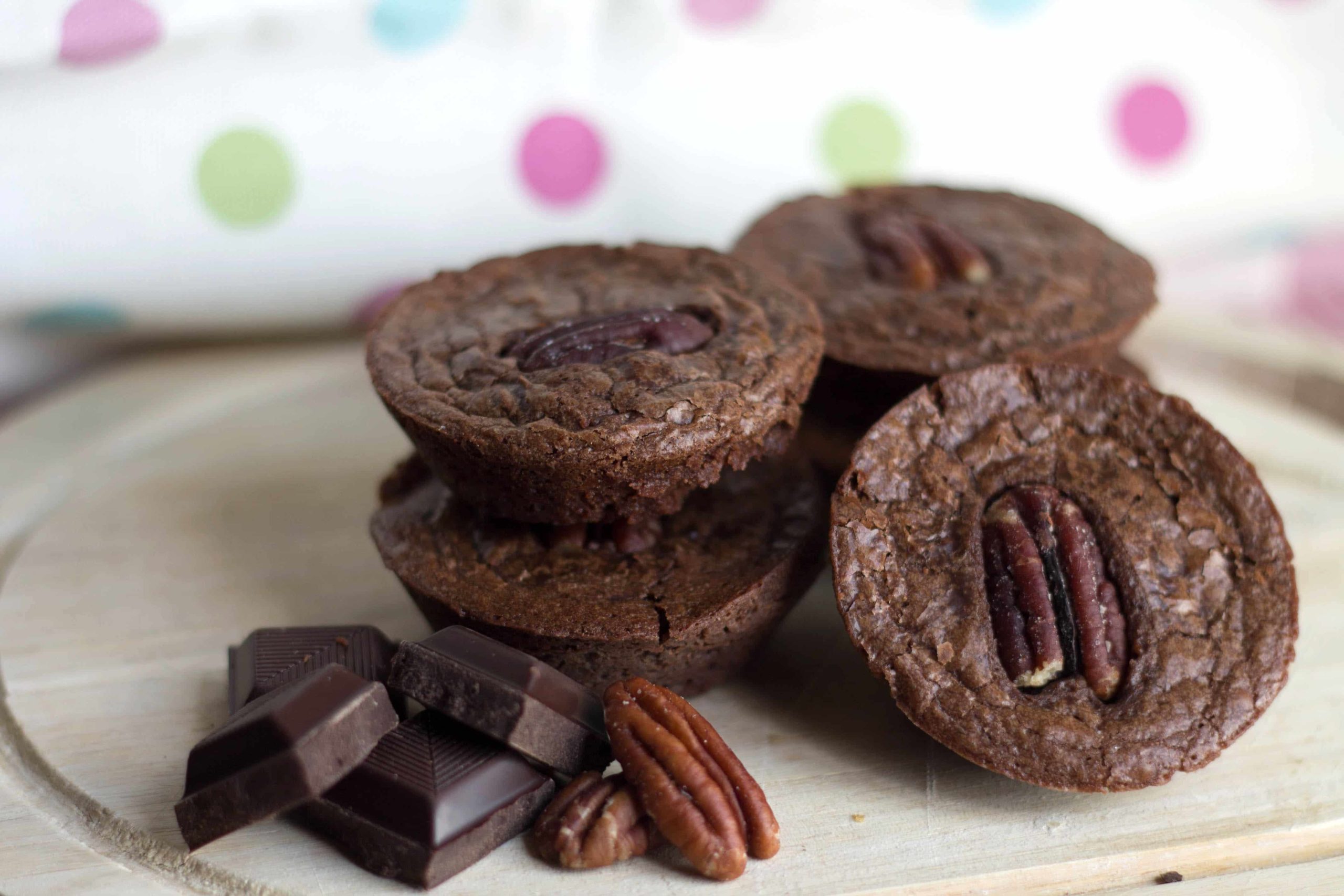 Triple Chocolate Brownie Bites on a plate with chunks of chocolate and pecans surrounding it