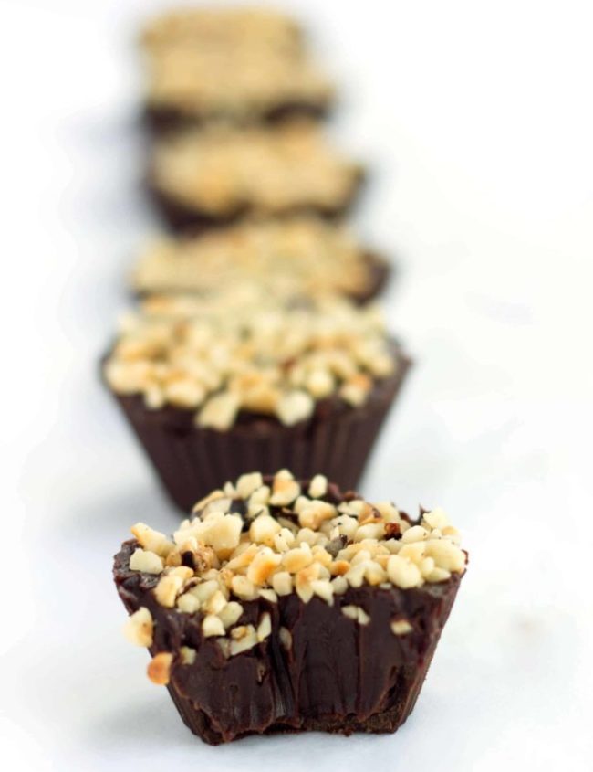 Close-up of Chocolate Hazelnut Truffle Cups topped with chopped nuts arranged in a row, with the focus on the front cup. The background is blurred, emphasizing the creamy texture and nutty topping of the chocolate truffle in the foreground.