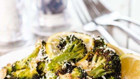 roasted broccoli piled high on a plate scattered with grated cheese and brown garlic