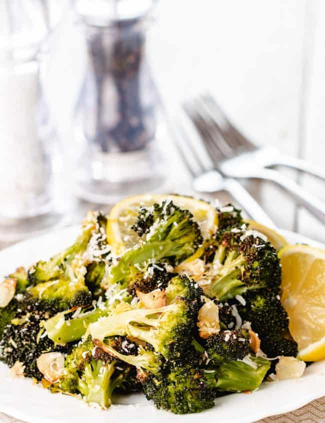 roasted broccoli piled high on a plate scattered with grated cheese and brown garlic