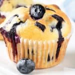 a blueberry muffin topped with a fresh blueberry with more muffins in the background