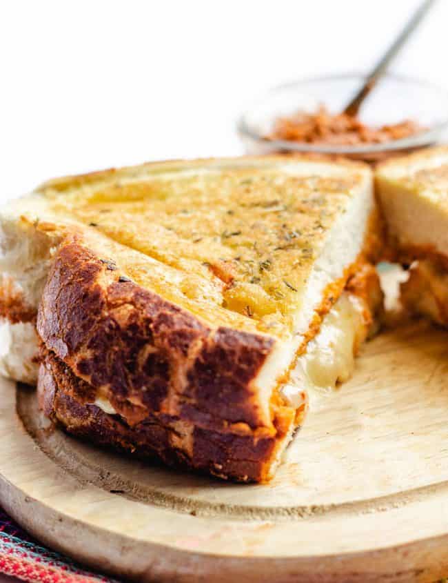 A golden grilled cheese sandwich on a cutting board with cheese oozing out of the middle