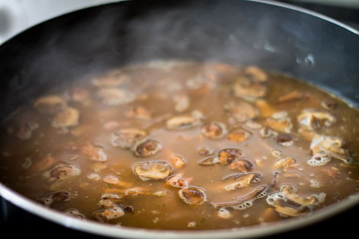 The stock and vermouth mixed into the rice mixture boiling in the pan 