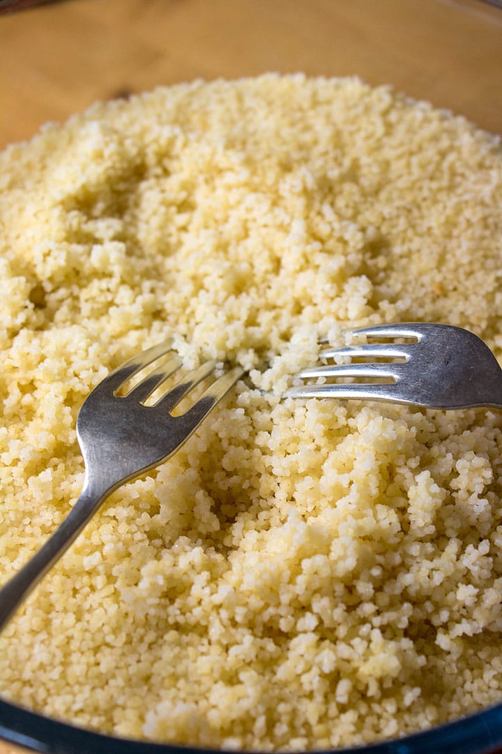 Two forks fluffing up the couscous in a large glass bowl