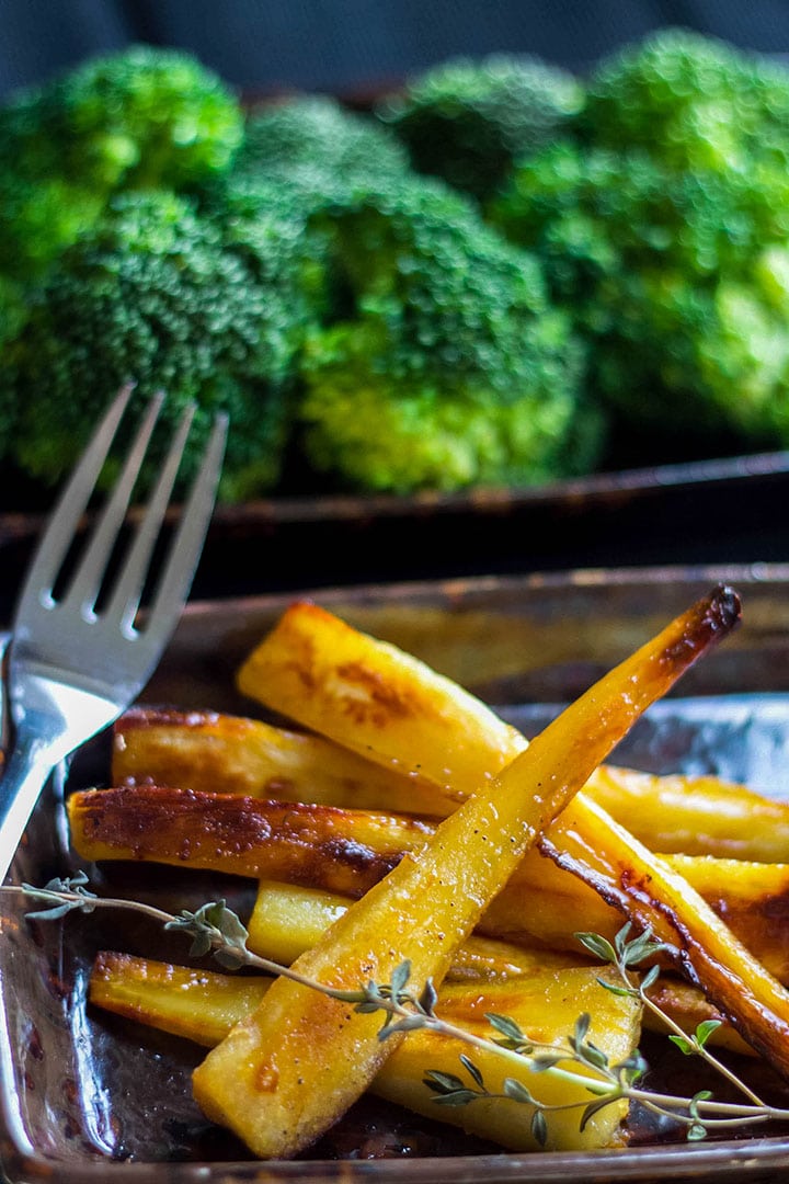 Honey & Maple Roasted Parsnips on a serving dish ready to eat with broccoli in the background