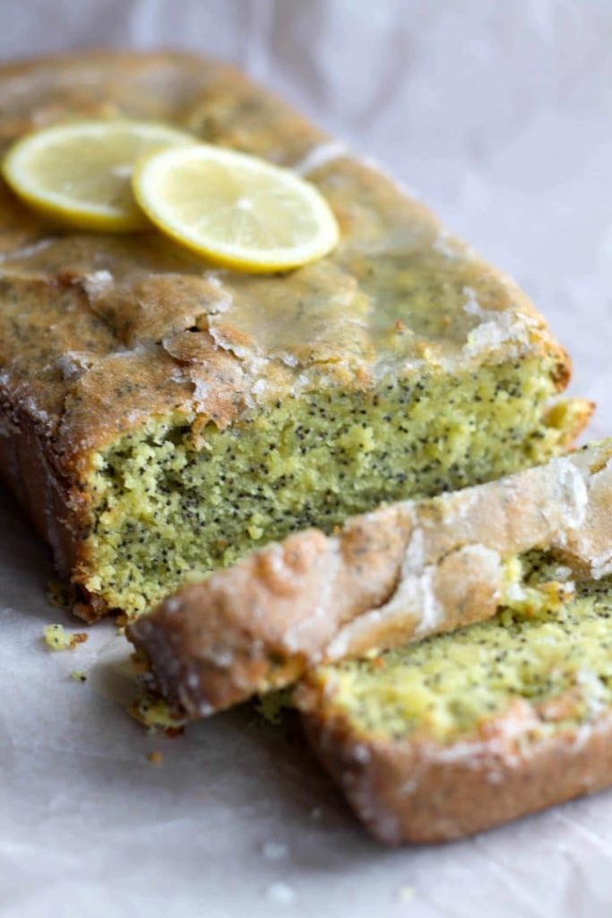 A close up of the Glazed Lemon Poppy Seed Loaf Cake topped with slices of fresh lemon with two slices cut from it