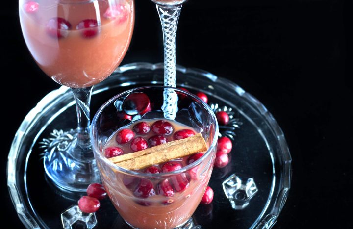 Cranberry, Orange & Cinnamon Cocktail in a glass with a cinnamon stick and fresh cranberries