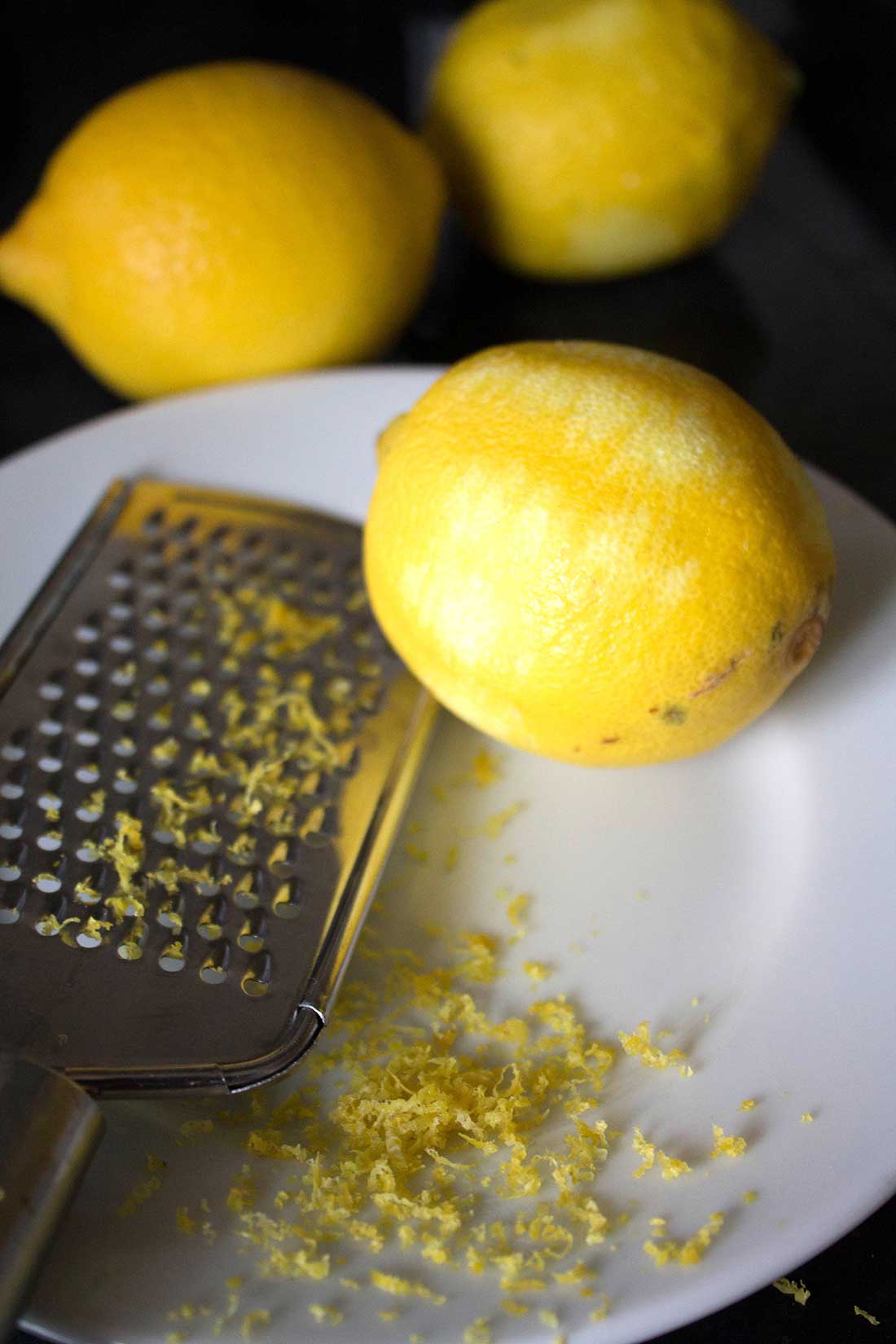 A lemon that's partially zested with the zest and zester next to it on a plate