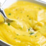 A bowl of bright yellow cauliflower soup in a white bowl