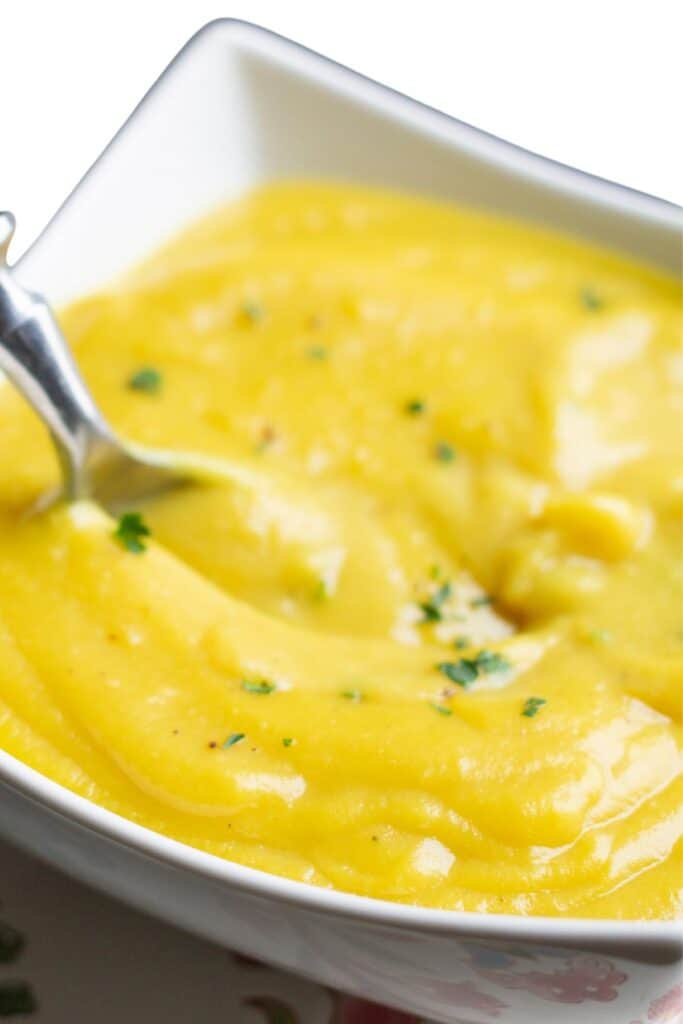 A bowl of bright yellow cauliflower soup in a white bowl