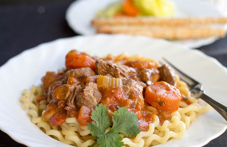 A plate of Italian Lamb Stew on a bed of pasta with a fork