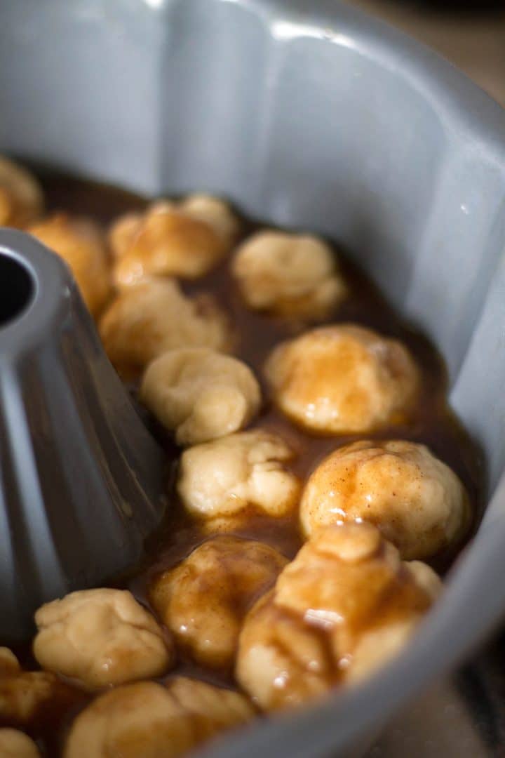 Balls of dough being placed in the sauce in a pan for the monkey bread