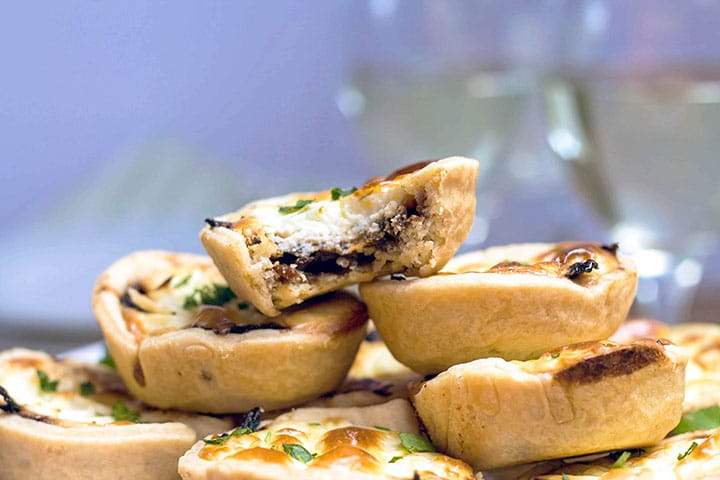 Feta and Caramelized Onion Tarts on a serving dish the top one with a bite taken out