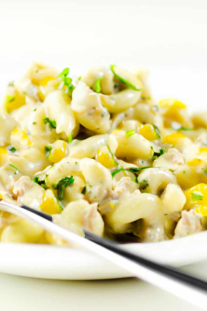 a plate piled high with tuna pasta salad with corn and herbs and a fork next to the plate