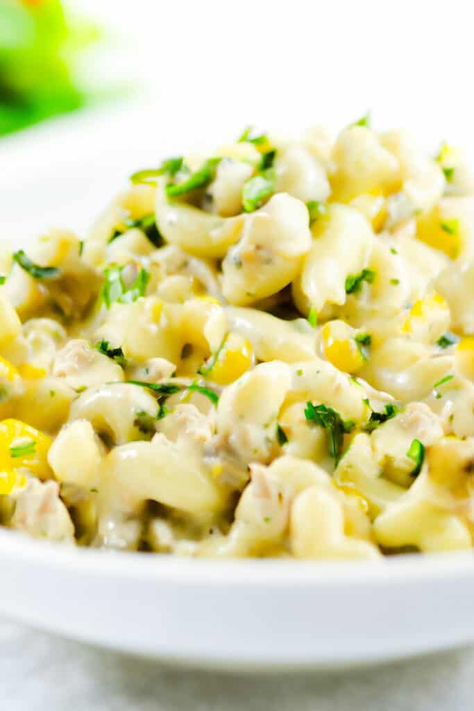 A bowl piled high with tuna pasta salad with corn, celery, and green onions.