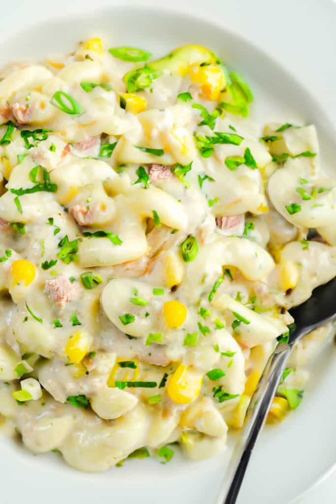 an overhead, close up shot of a bowl of tuna pasta salad with celery, scallions, and chopped herbs.