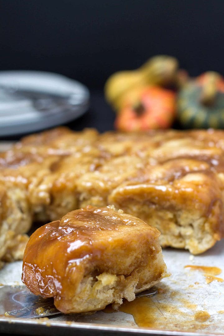 A tray of gooey pumpkin spice sticky buns with one pulled out to show the filling