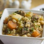 A square white bowl of beef and barley soup