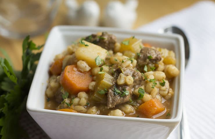 A square white bowl of beef and barley soup