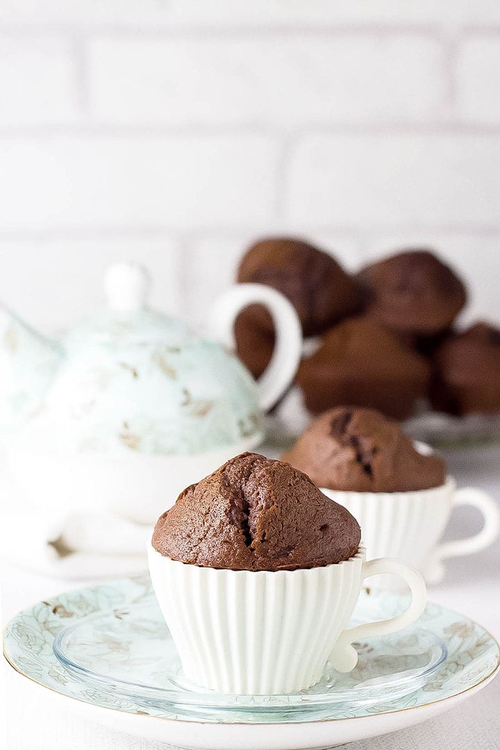 A Double Chocolate Chip Muffin in a tea cup muffin case with a teapot and more muffins in the background