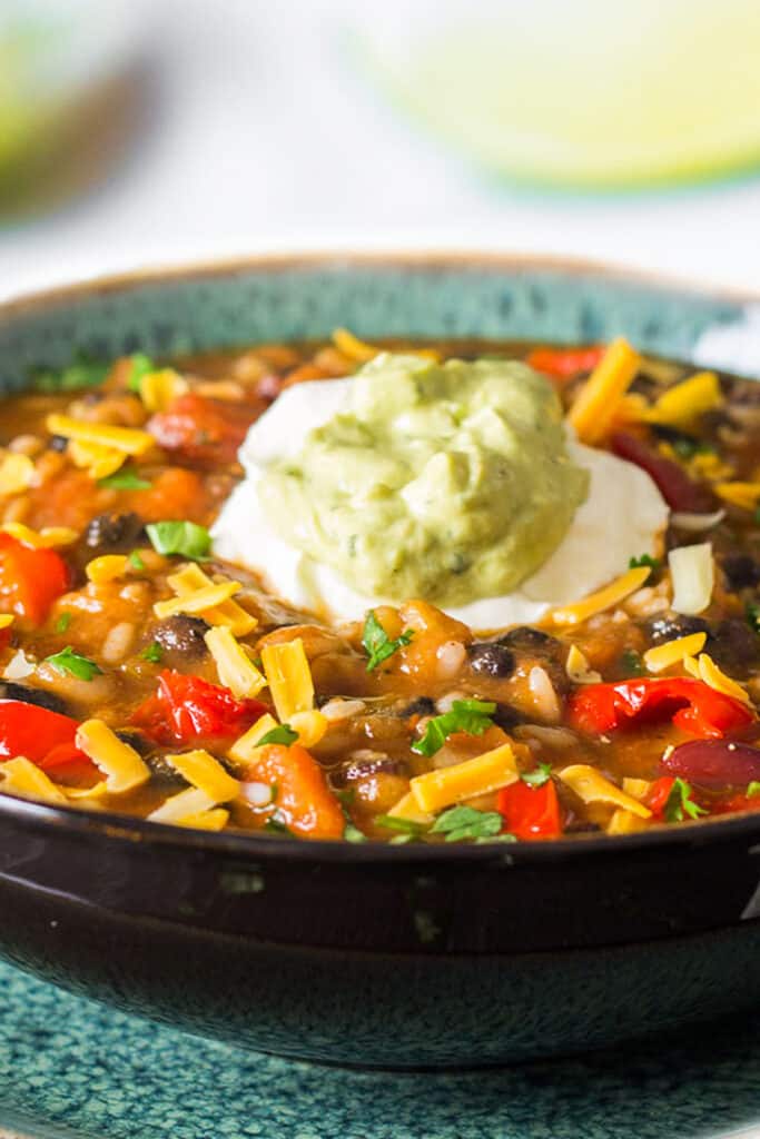 a big bowl of Mexican soup topped with cheddar cheese, sour cream and Guacamole