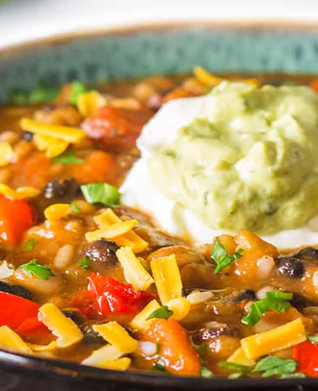 a bowl of Mexican soup topped with Guacamole and sour cream