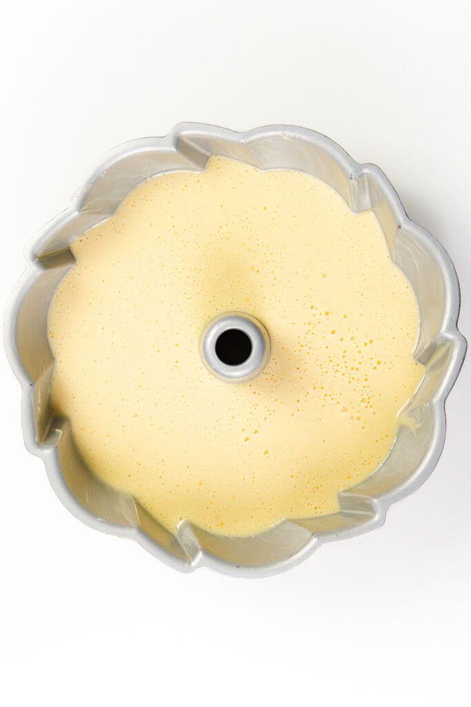 A Bundt pan filled with smooth, creamy citrus cake batter, infused with olive oil, ready for baking. The light yellow batter is evenly distributed in the pan, highlighting its decorative scalloped edges.