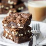 three triple chocolate chip bars on a plate with a fork and a glass mug of coffee in the background