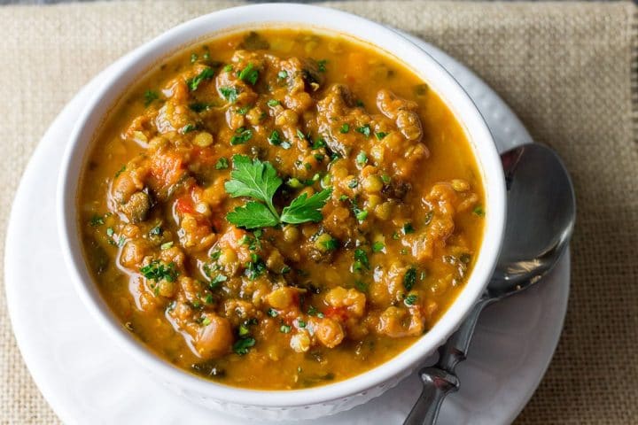 A close up of Homemade Lentil Soup piled with lentils topped with parsley