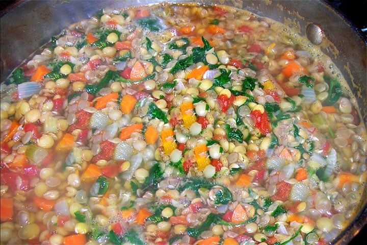 A close up of the the lentils, stock, parsley, carrots and onions before cooking down into the soup