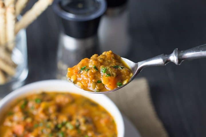 A close up of a spoon full of Homemade Lentil Soup with the bowl beneath it