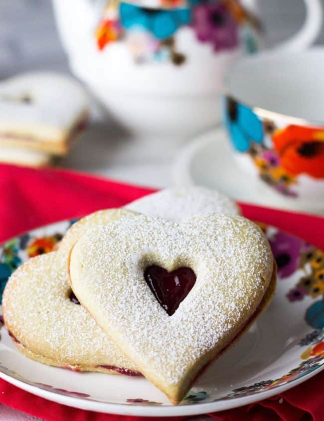 two Raspberry Butter Cookies on a plate dusted with powdered sugar