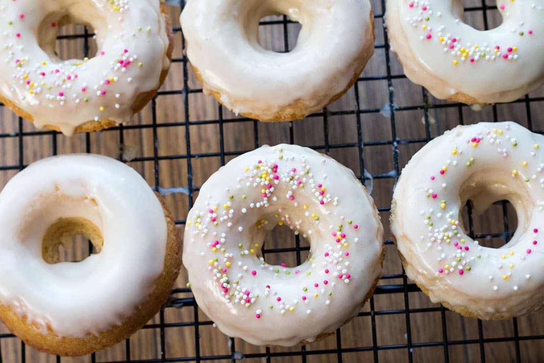 The Baked Iced Vanilla Doughnuts on a cooling rack half with sprinkles and half with just icing.