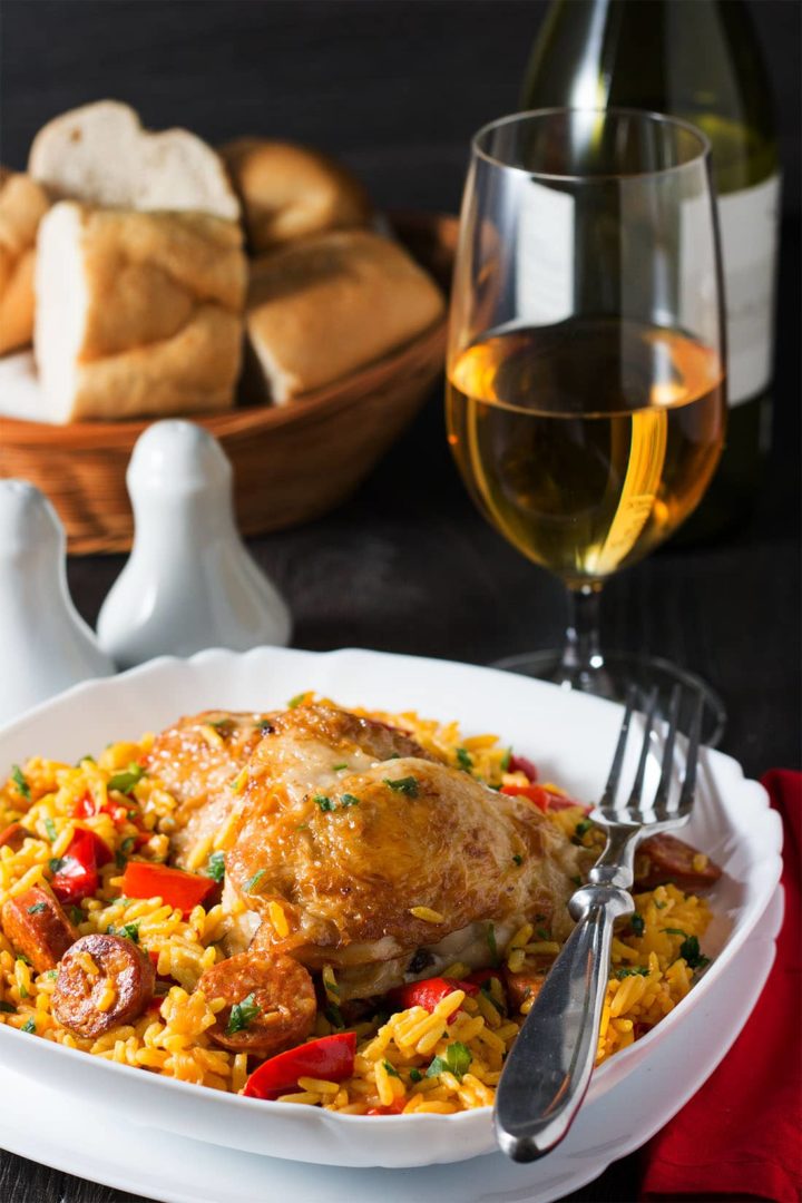 A close up of the golden chicken on the yellow saffron rice with slices of sausage and red peppers