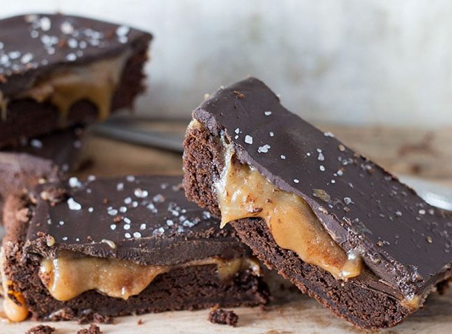 Cut slices of the Salted Chocolate & Caramel Bars stacked and piled on each other with the caramel oozing out and the salt on top