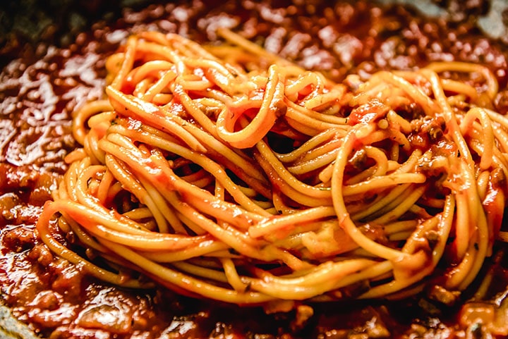 spaghetti added to the sauce in the pan