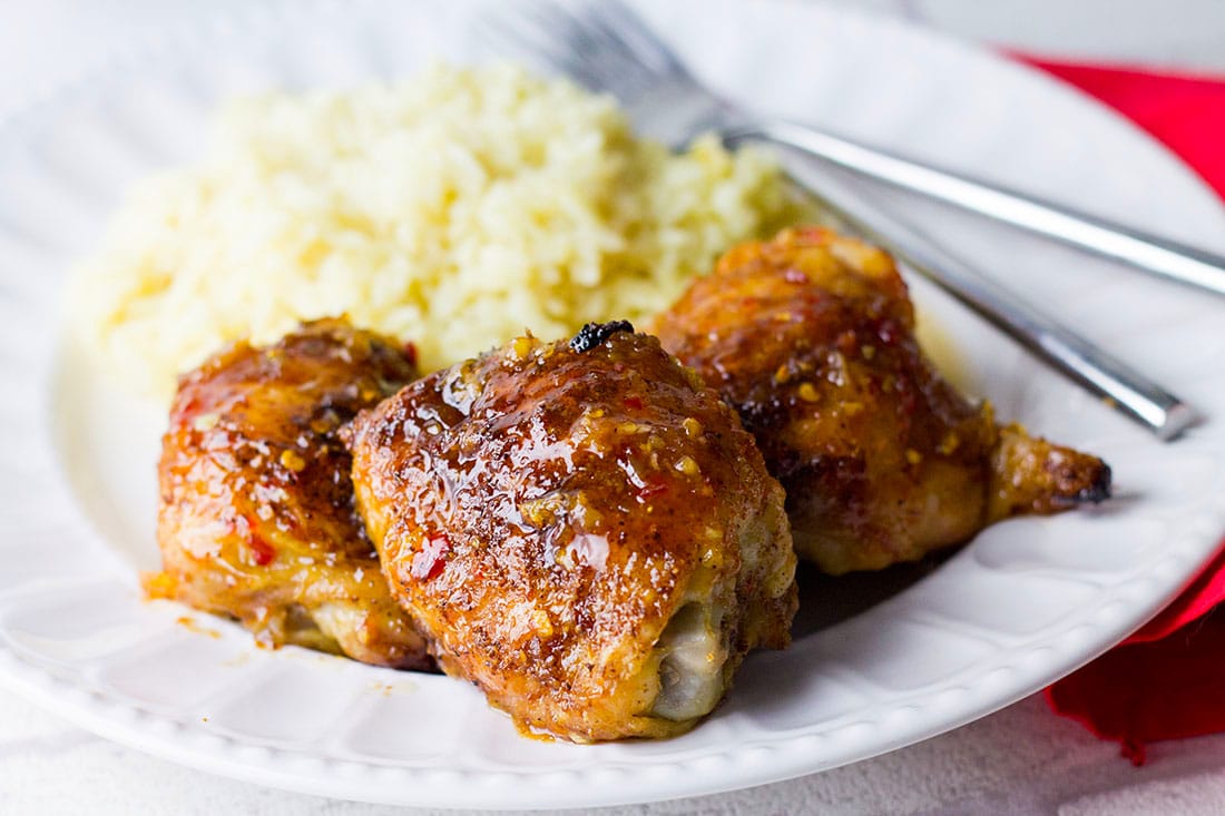 The Sweet Chilli Chinese Sticky Chicken with it's shiny sauce with bits of garlic and ginger and a mound of rice on the plate beside it.