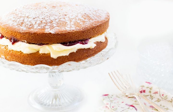 Classic Victoria Sponge Cake on a glass cake stand with a floral napkin and a silver fork next to it