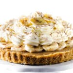 The Banoffee Pie on a cake stand showing the crust, caramel layer, banana layer, whipped cream and banana chips as decoration.